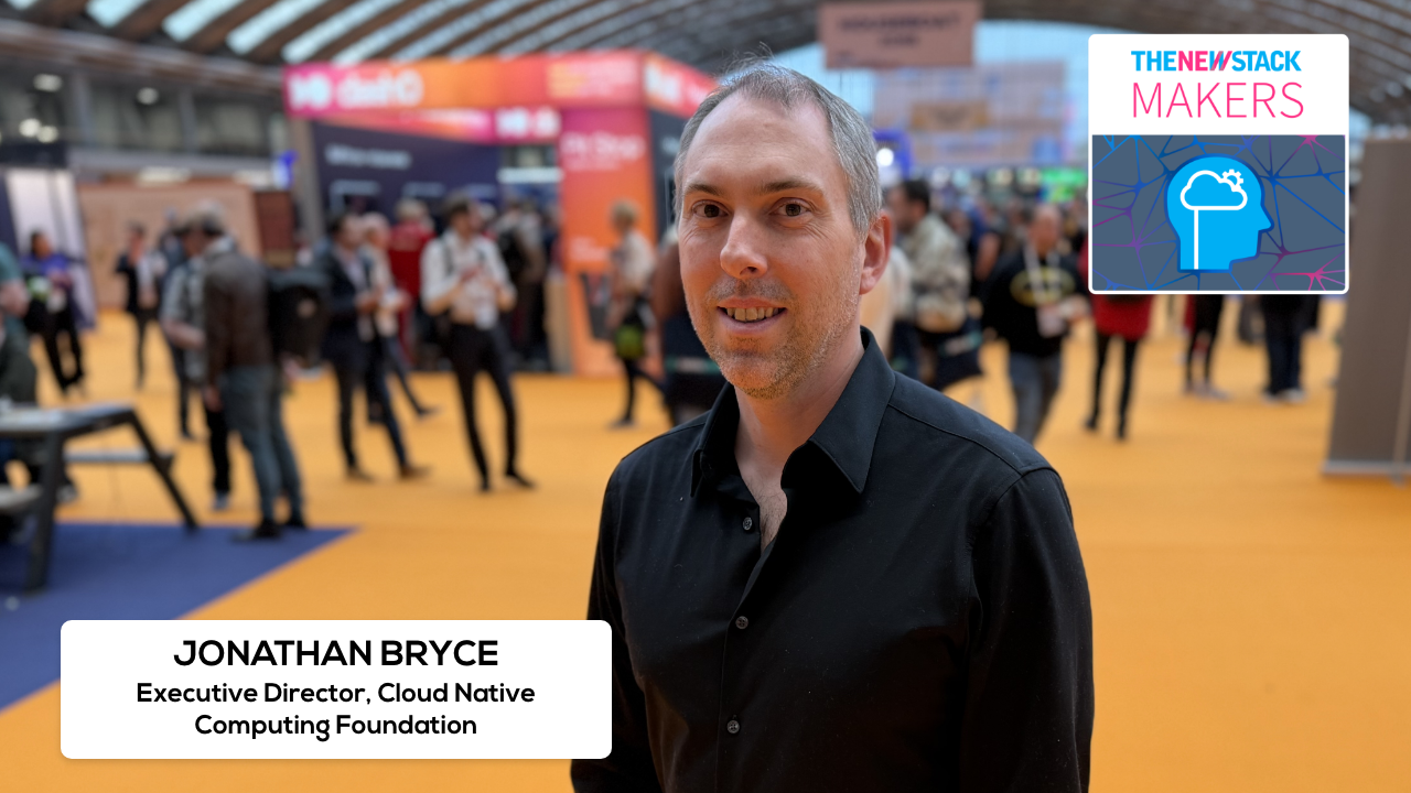 Jonathan Bryce speaking at KubeCon Amsterdam on Kubernetes AI conformance stage with crowd and screens